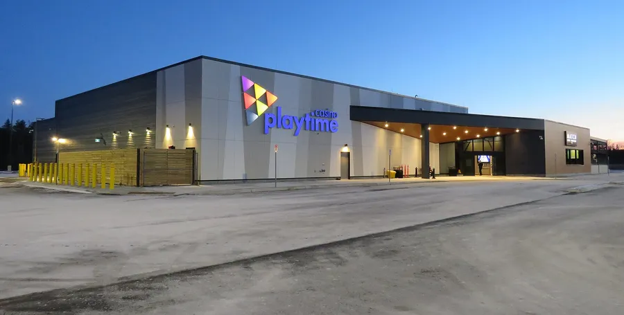 Photograph: the low grey casino building on Joseph Drive at dusk, its sign lit, with a long entrance canopy and an empty parking lot.